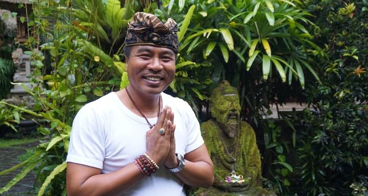 Mann in traditioneller Kleidung grüßt vor Grünzeug.