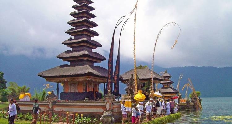 Grupo realizando una ceremonia cerca de un templo tradicional junto al agua en Indonesia.