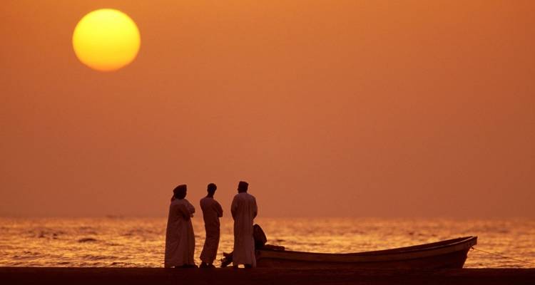 A silhouetted group of people with a boat at sunset.