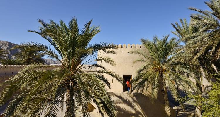 A fort with palm trees and people walking about.