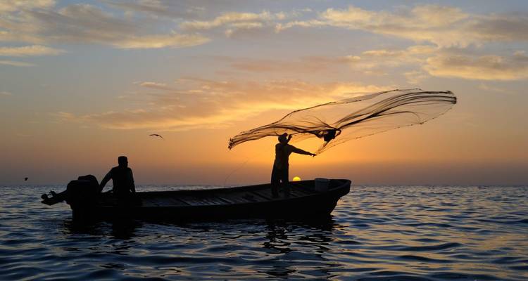 Dramatic sunset scene with fishermen on a boat casting a net.