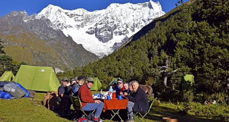 Group of people dining at a campsite with mountains in the background.
