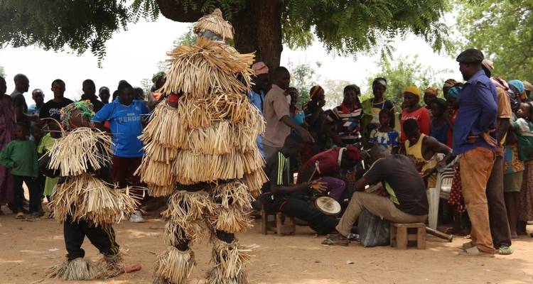 Cultural performance with people wearing straw costumes in a village setting.
