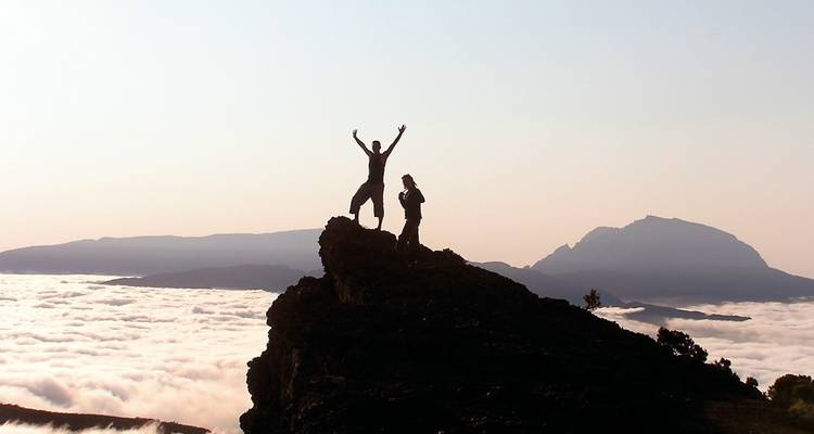 Two people on a rocky peak above the clouds.