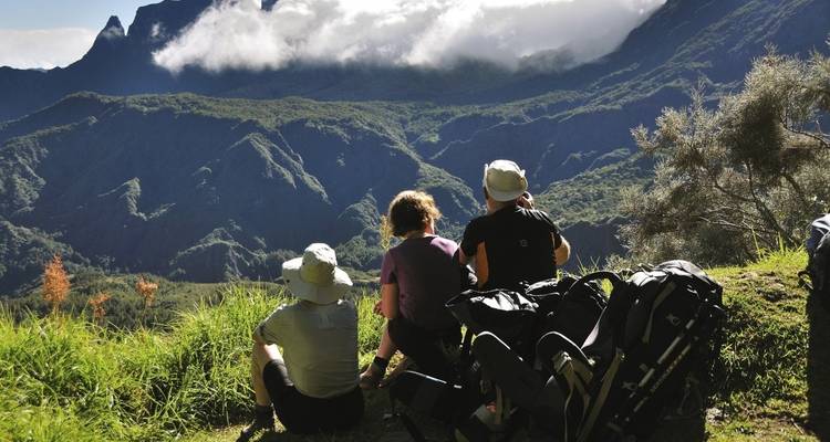 Three people resting with backpacks, overlooking a mountainous landscape.