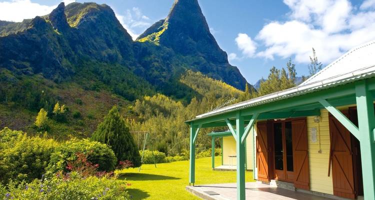 House with a mountain backdrop under a sunny sky.
