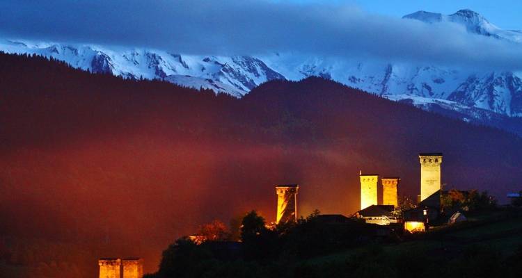 Torres defensivas iluminadas con un telón de fondo montañoso al anochecer.