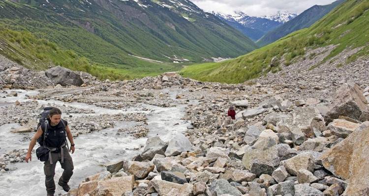 Excursionistas cruzando un lecho rocoso de río con montañas verdes alrededor.