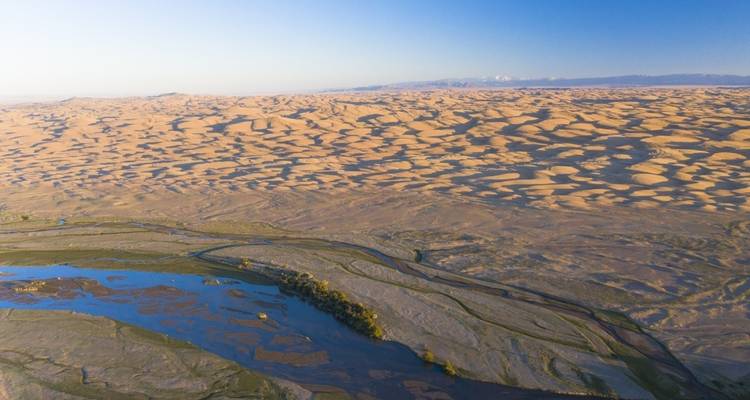 Luftaufnahme von weitläufigen Sanddünen mit Gewässern im Vordergrund.