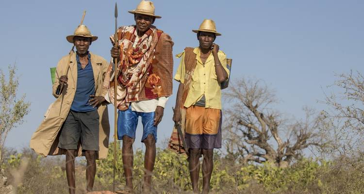 Three people standing outdoors, wearing hats and traditional attire.