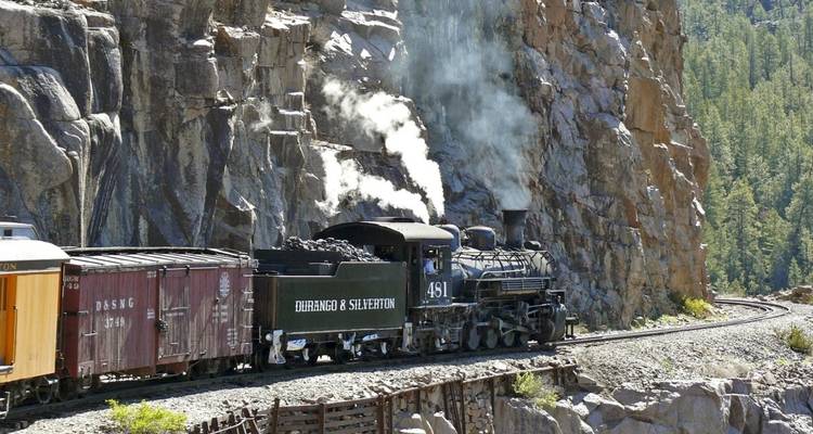 Steam train winding through a rocky mountain landscape.