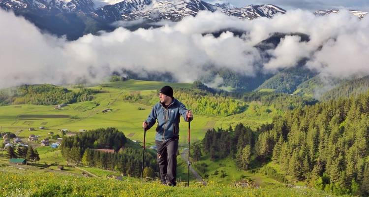 Homme faisant de la randonnée à travers un paysage verdoyant luxuriant avec des montagnes et des nuages.
