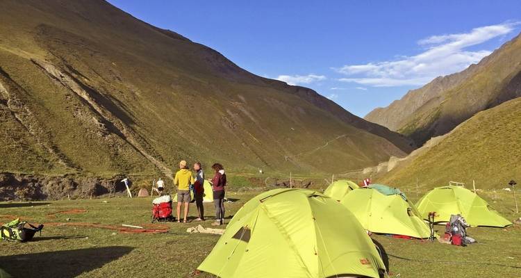 Des gens qui installent un campement dans une vallée avec des montagnes vertes.