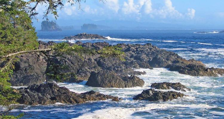 Côte rocheuse avec des vagues qui se brisent et des îles au loin.