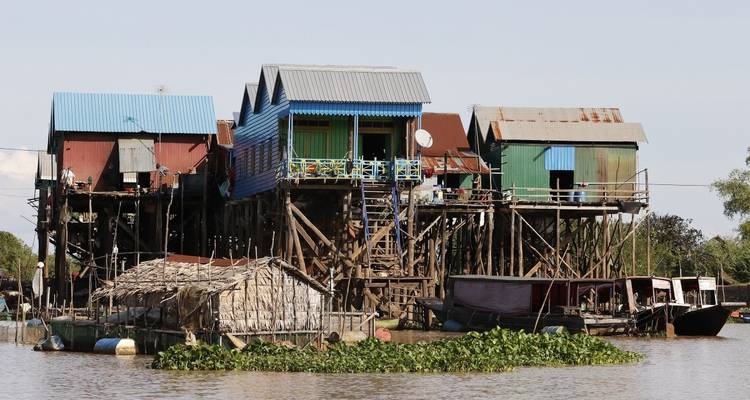 Maisons sur pilotis en bois au bord d'une rivière avec de petites embarcations.
