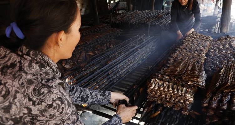 Des femmes qui grillent du poisson sur un barbecue au charbon de bois.