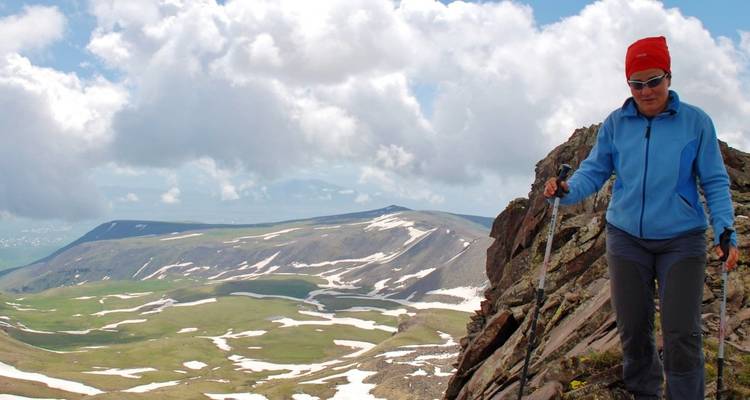 A hiker on a rocky cliffside with snow patches and a vast landscape.