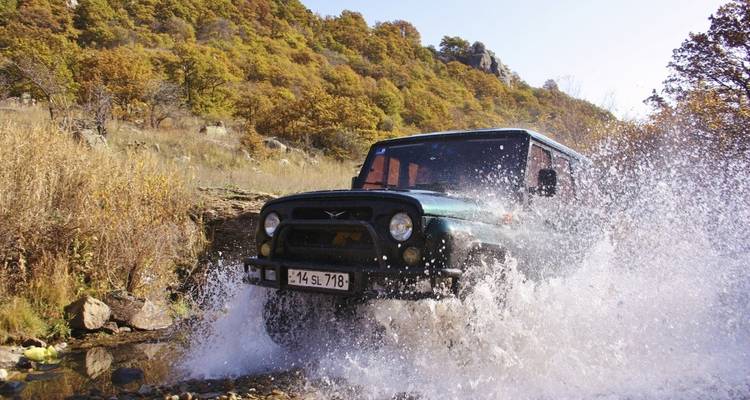 A vehicle splashing through a stream in a forested area.