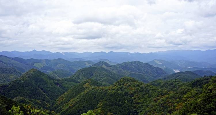 Vue panoramique de montagnes verdoyantes sous un ciel nuageux.