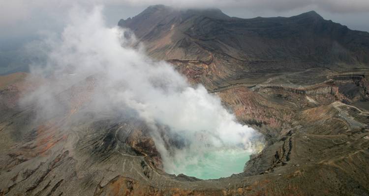 Cratère de volcan émettant de la vapeur avec terrain accidenté environnant.