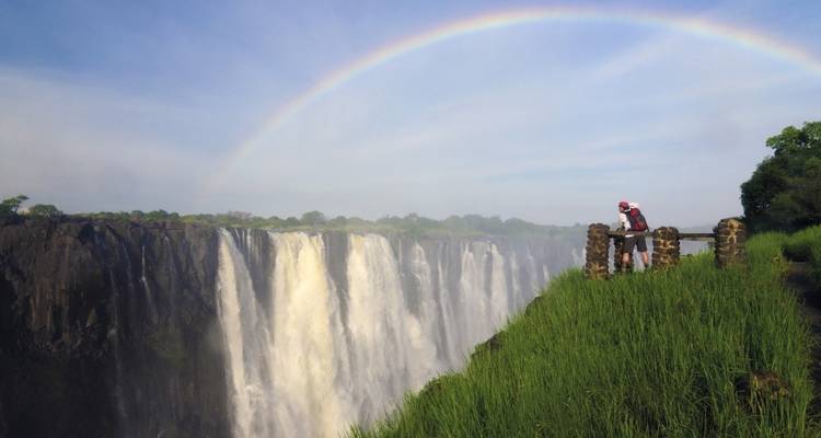 "Las Cataratas Victoria con un arcoíris y una persona observándolas."