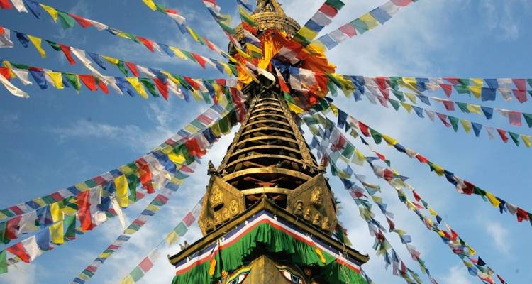 Stupa with colorful prayer flags under a blue sky.