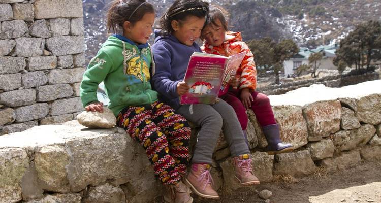 Trois enfants assis sur un mur de pierre en train de lire un livre.