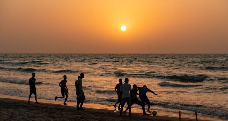 Siluetas de personas jugando fútbol en una playa al atardecer.