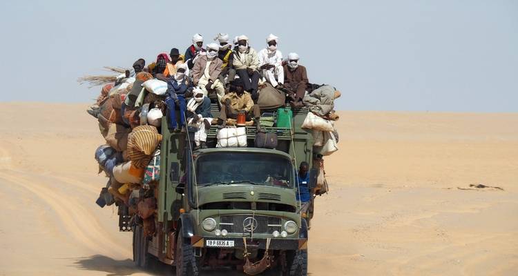 A truck overloaded with people and goods driving through the desert.