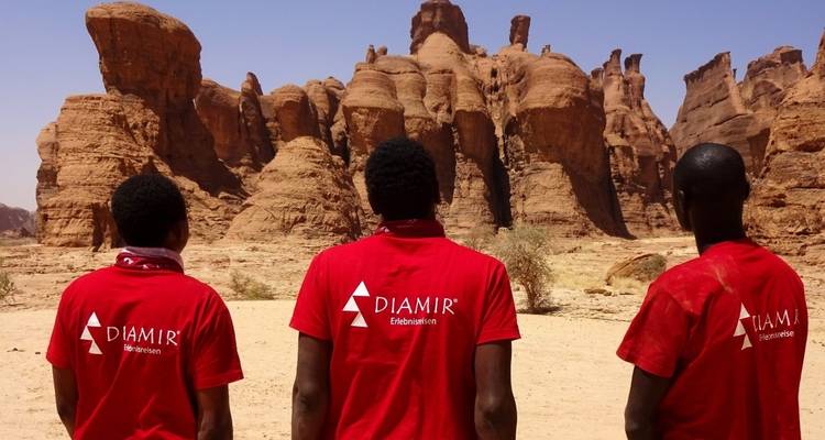 Three people facing a rock formation in the desert.