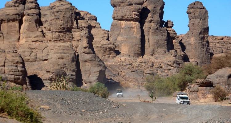 Vehicles driving through a rocky desert landscape.