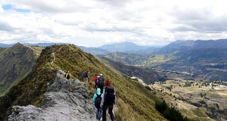 Eine Gruppe von Wanderern, die einen schmalen Grat überqueren und dabei einen Panoramablick auf Hügel haben.