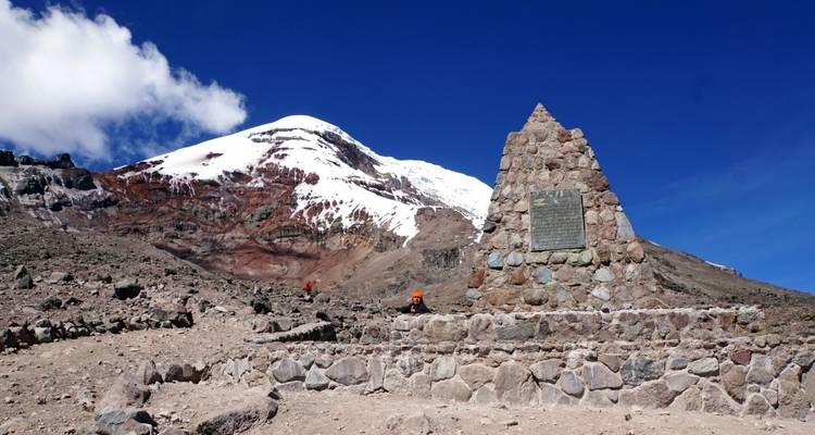 Ein Steinmonument am Fuß eines schneebedeckten Berges unter einem klaren Himmel.