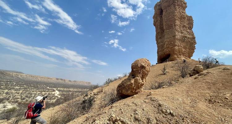Photographer takes aim at a towering desert rock pillar rising against a bright sky.