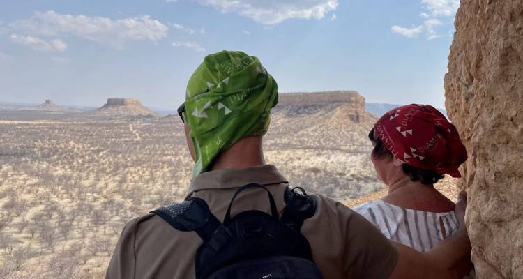 Travelers look out from a cave window onto vast flat-topped mesas and arid plains.