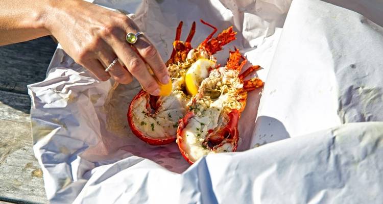 Gros plan d'une main pressant un citron sur un homard cuit posé sur du papier blanc.
