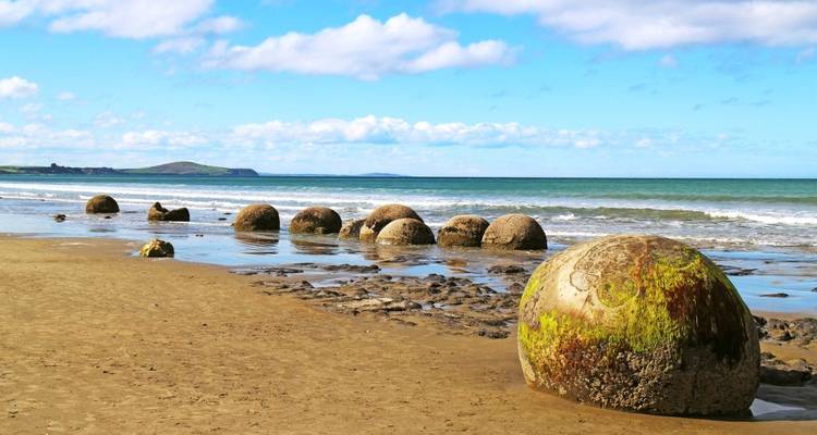 Rochers de Moeraki sur une plage de sable avec l'océan en arrière-plan.