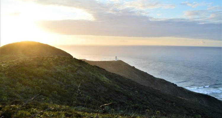 Un phare sur une falaise avec vue sur l'océan au coucher du soleil.