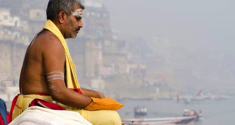 Eine Person, die an einem Flussufer mit Stadtsilhouette meditiert.