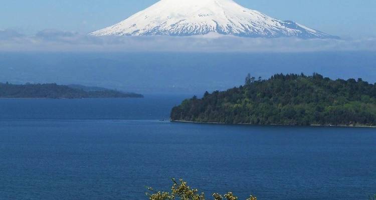 Volcán cubierto de nieve sobre un lago azul y un bosque exuberante.