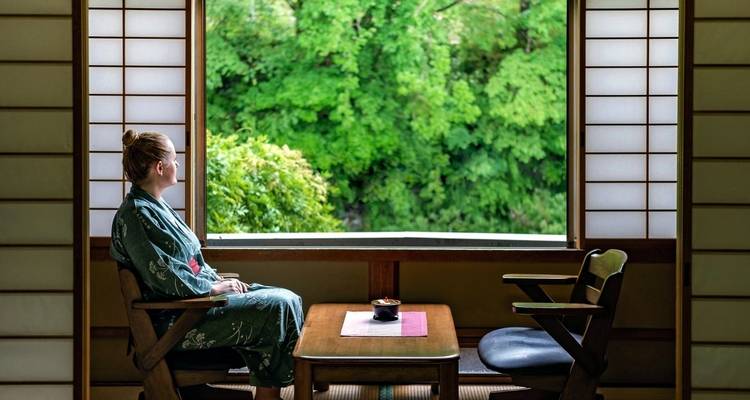 Person in traditionellem Kimono sitzt drinnen mit Blick auf die Natur.