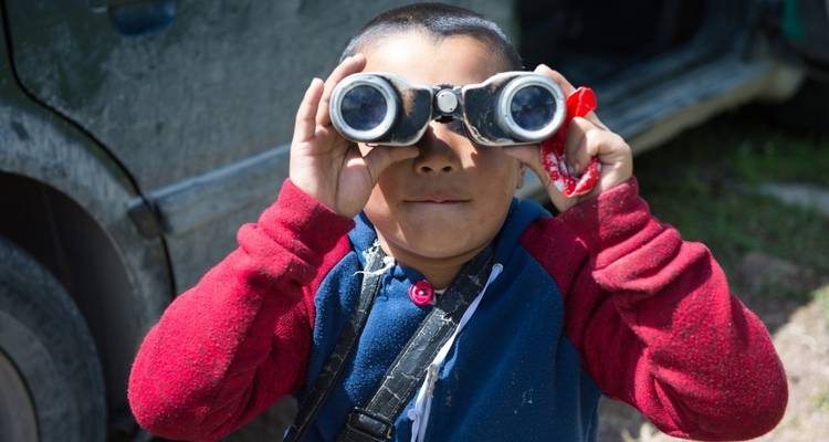 Child looking through binoculars with a playful expression.