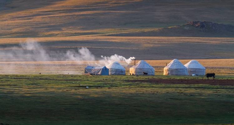 Yurts in a wide open landscape with smoke rising and hills in the background.