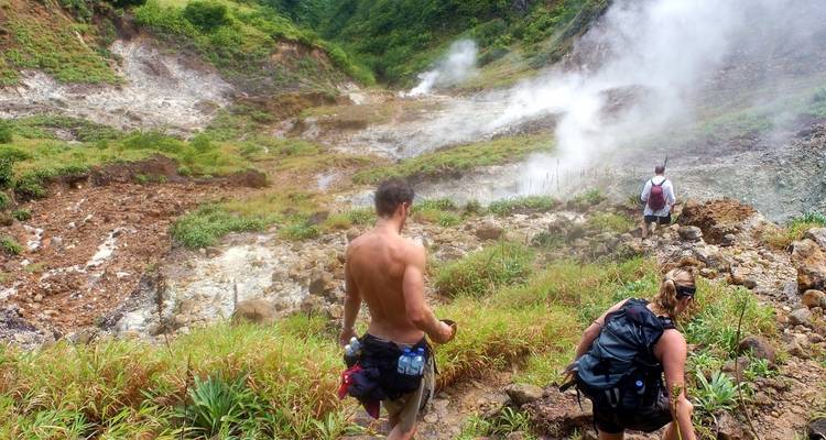 Excursionistas explorando una zona geotermal humeante en un paisaje montañoso.