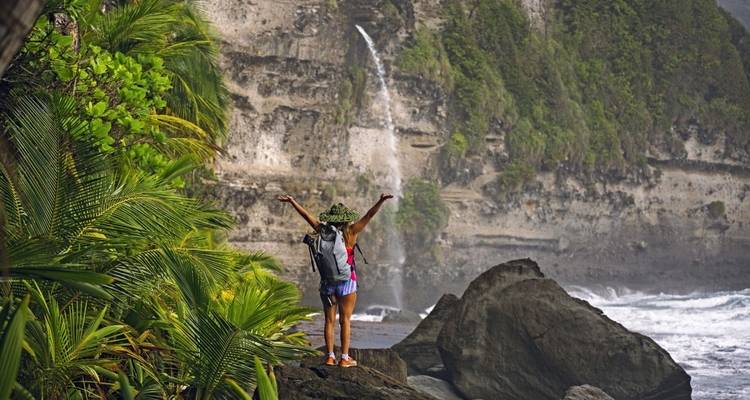 Un excursionista con los brazos levantados parado junto a una orilla rocosa con una cascada.