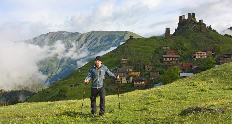 Una persona haciendo senderismo con bastones de trekking cerca de un pueblo montañoso.