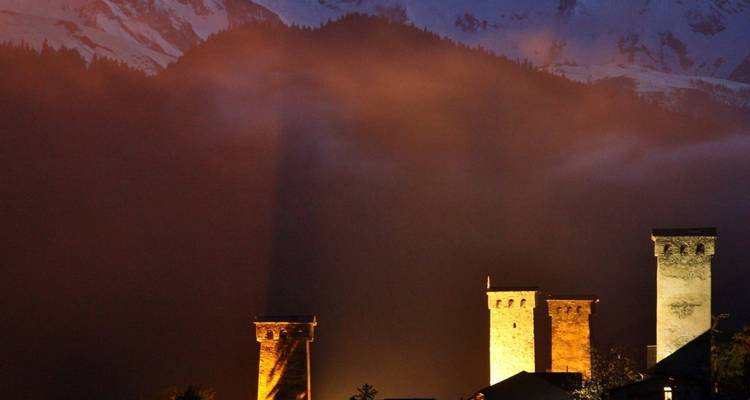 Torres iluminadas con montañas y nubes de fondo.