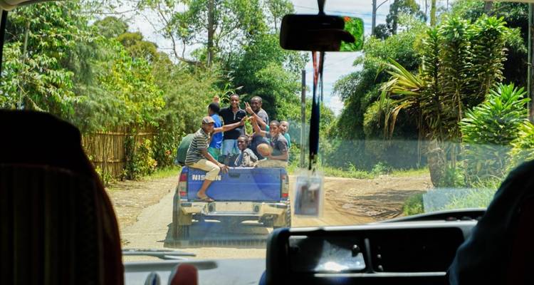 View through a vehicle of a group of people riding on a pickup truck.