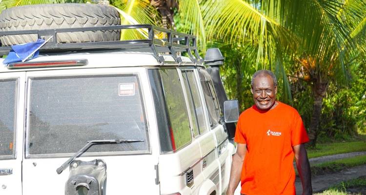 Man standing beside a vehicle with palm trees in the background.