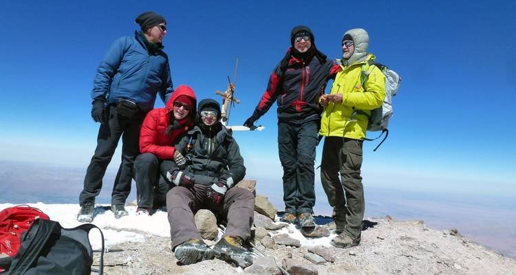 Group of climbers holding a cross on a snowy mountain peak.